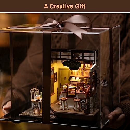 Person holding a miniature dollhouse in a gift box with a ribbon.