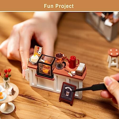 Hands arranging a miniature kitchen set with tiny furniture and utensils.